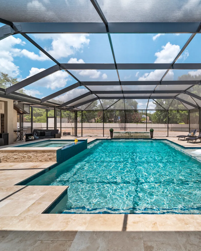 Custom pool with a stacked stone water wall and ivory travertine decking built by Pool Perfection in Odessa