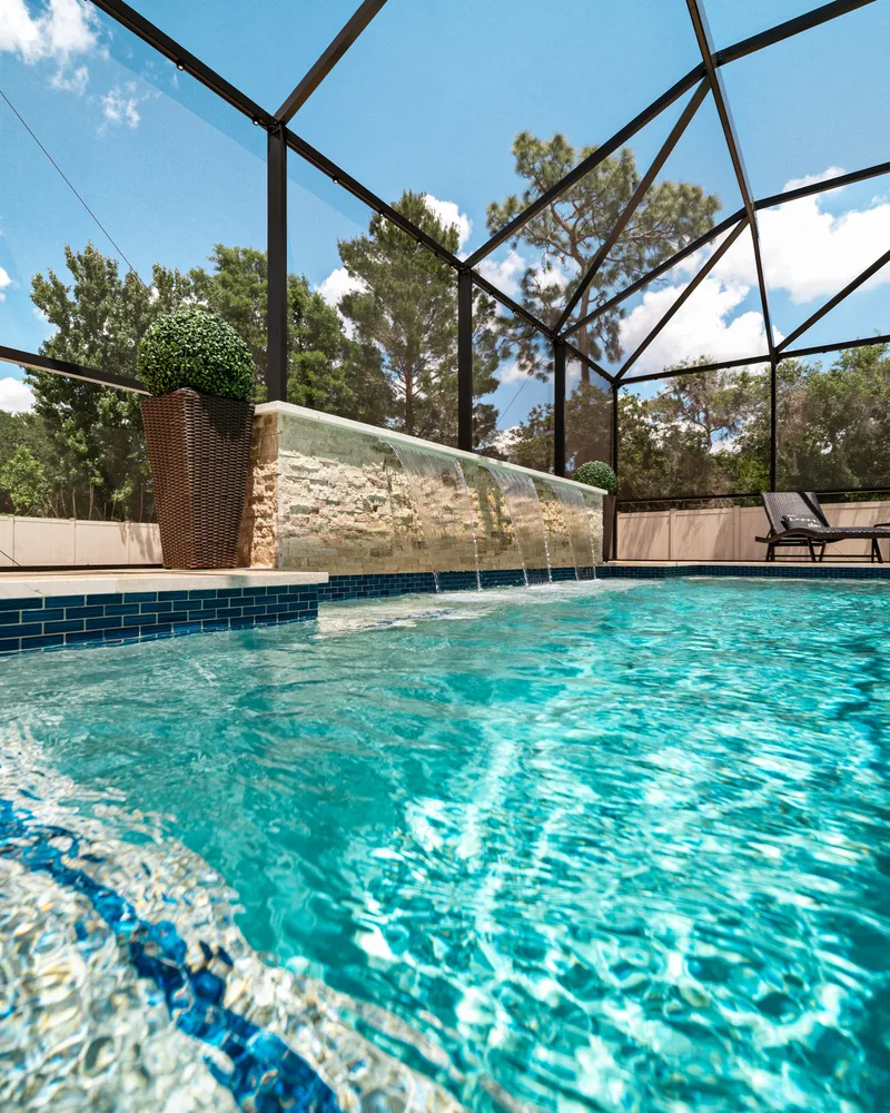 Custom pool with a stacked stone water wall and ivory travertine decking built by Pool Perfection in Odessa