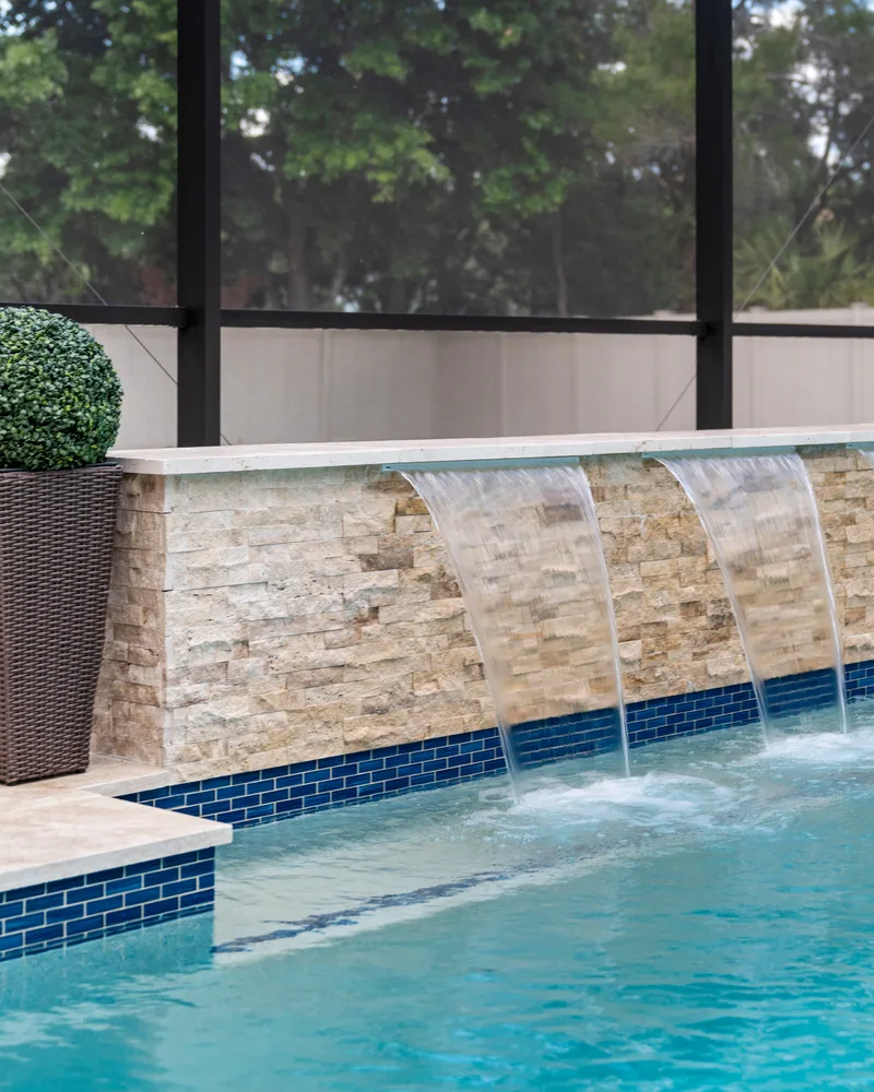 Custom pool with a stacked stone water wall and ivory travertine decking built by Pool Perfection in Odessa