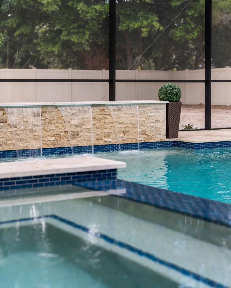 Custom pool with a stacked stone water wall and ivory travertine decking built by Pool Perfection in Odessa