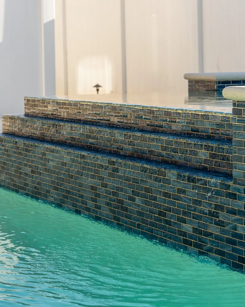 Custom pool with a water cascade and navy waterline tile built by Pool Perfection in Seminole